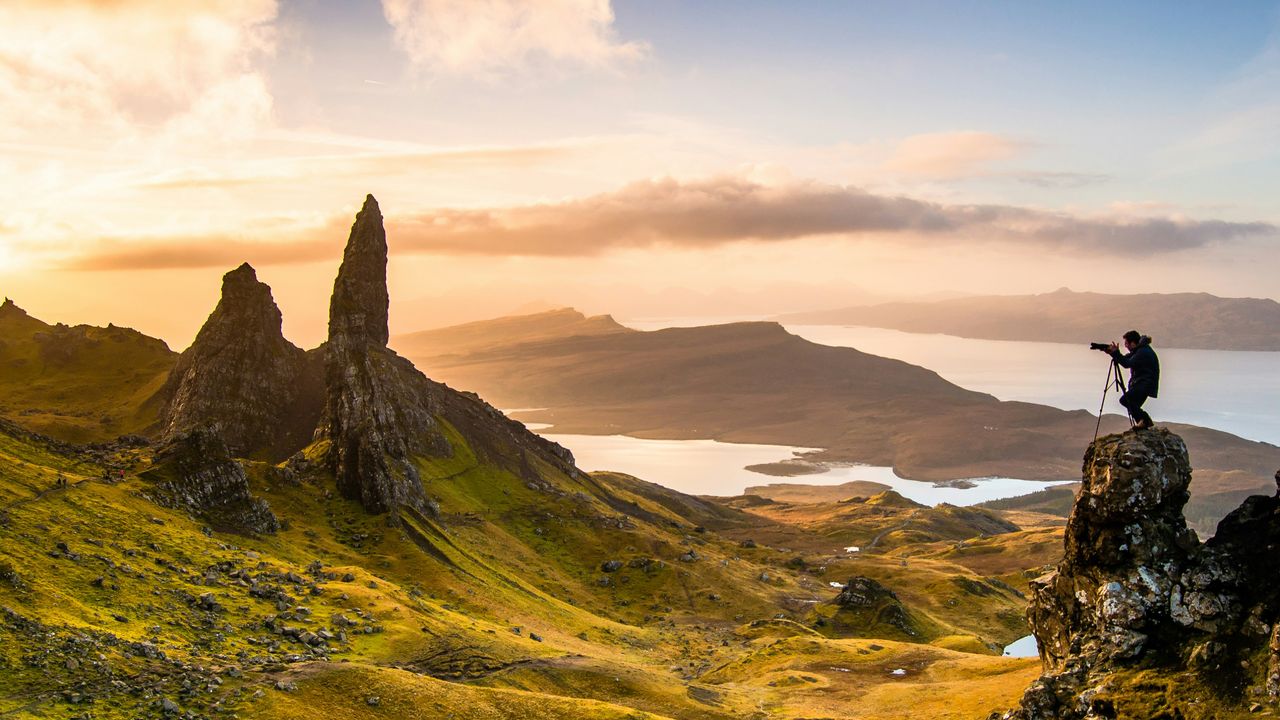 Photographer capturing magic hour photography on mountain peak with golden hour light and scattered clouds at sunset